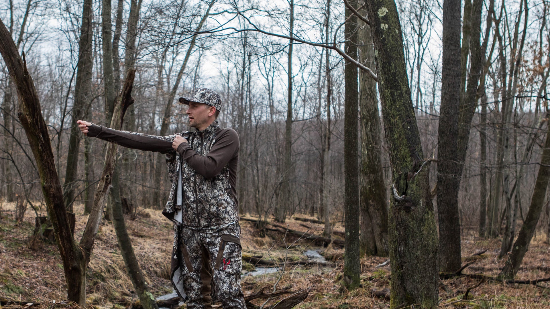 man putting on hunting jacket in the forest