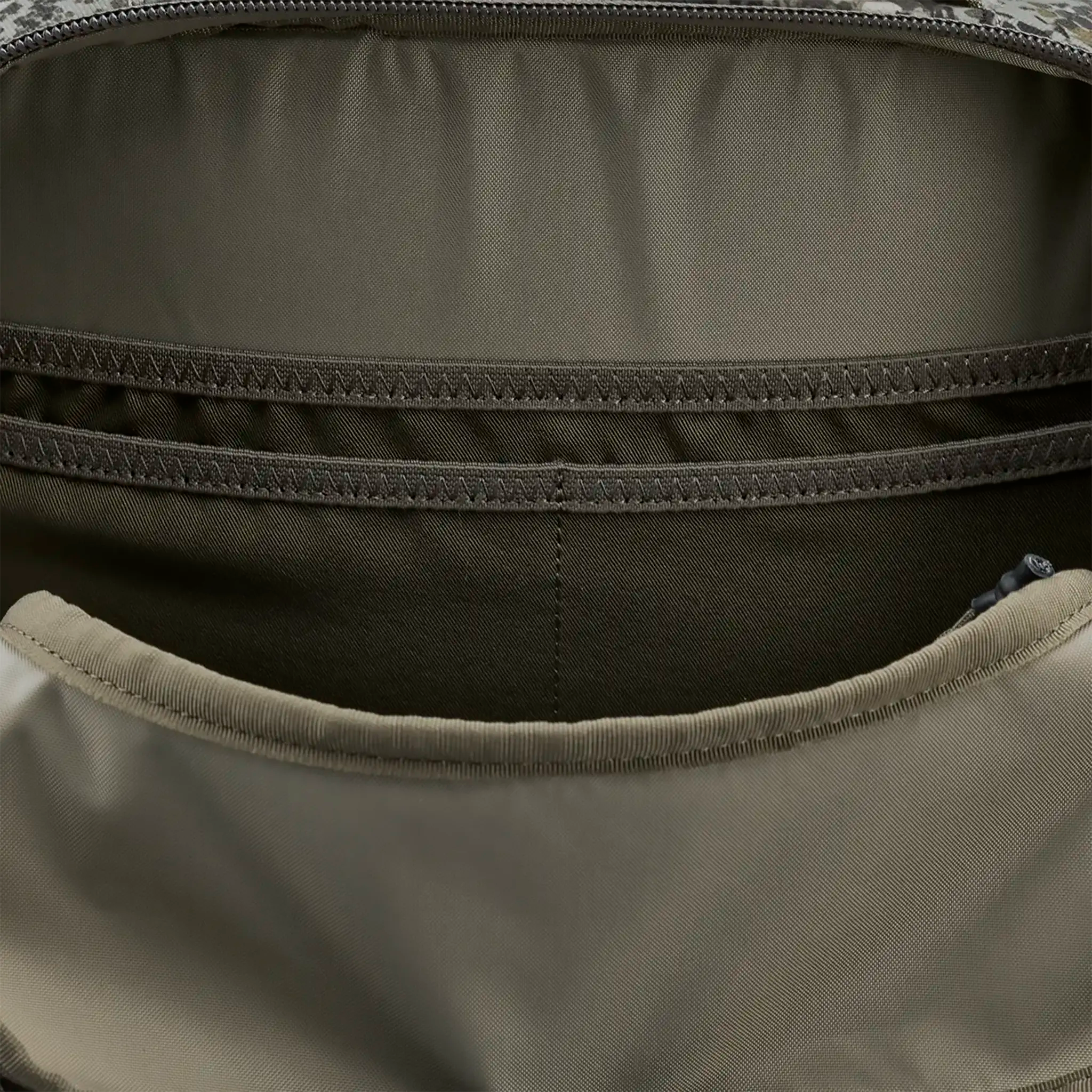 Close-up of an empty, tan and brown backpack interior with multiple stitched pockets and compartments.