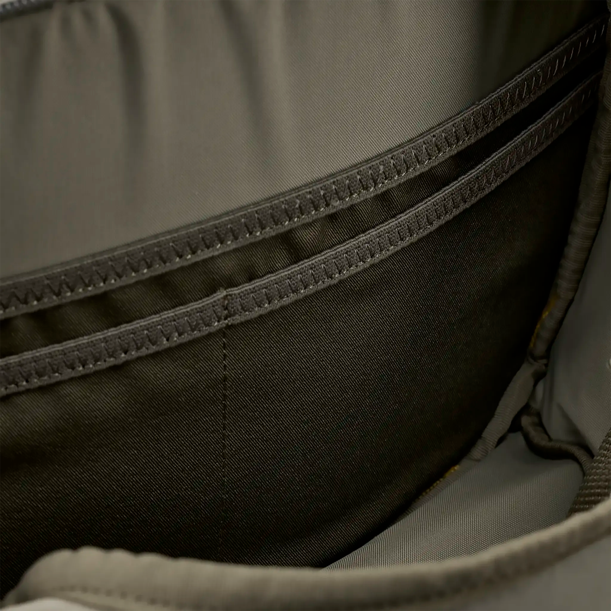 Close-up of an empty, khaki backpack interior showing two stitched pockets and smooth fabric lining.