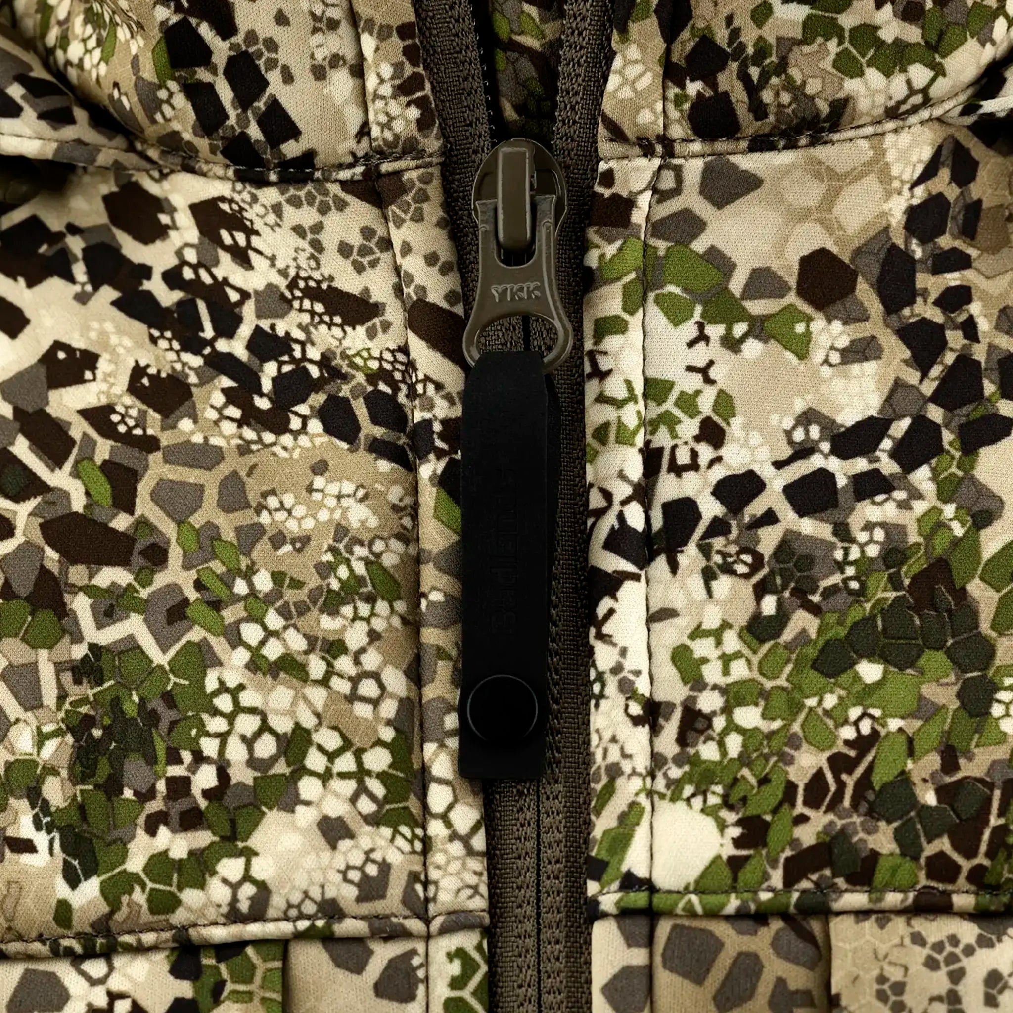 Close-up of a camouflage jacket zipper with a YKK pull tab, showing green, brown, and beige geometric patterns.