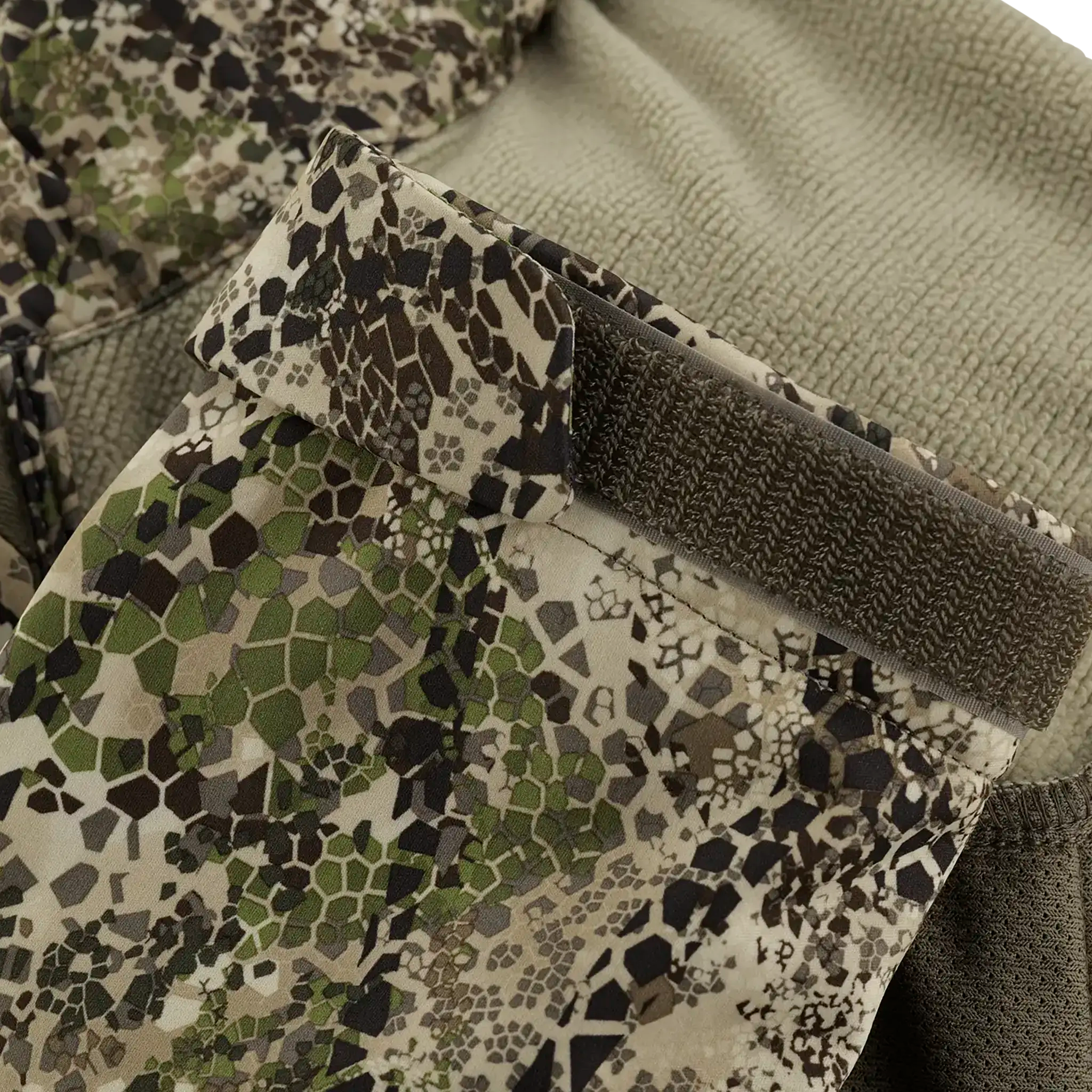 Close-up of a camouflage sleeve with a Velcro strap, featuring green, brown, and beige hexagonal patterns.