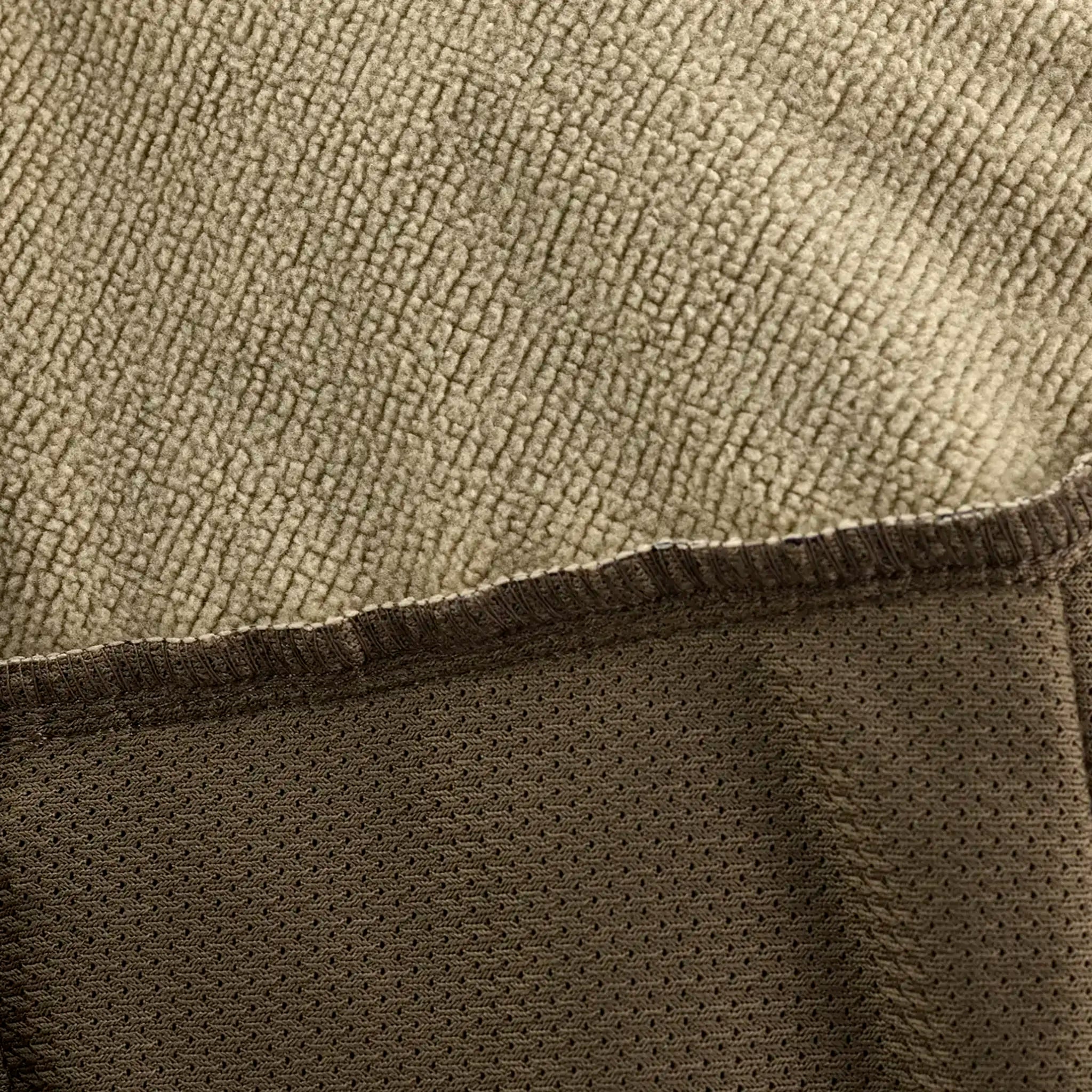Close-up of tan fleece fabric with brown mesh trim, showing texture and stitching details. No logos or graphics visible.