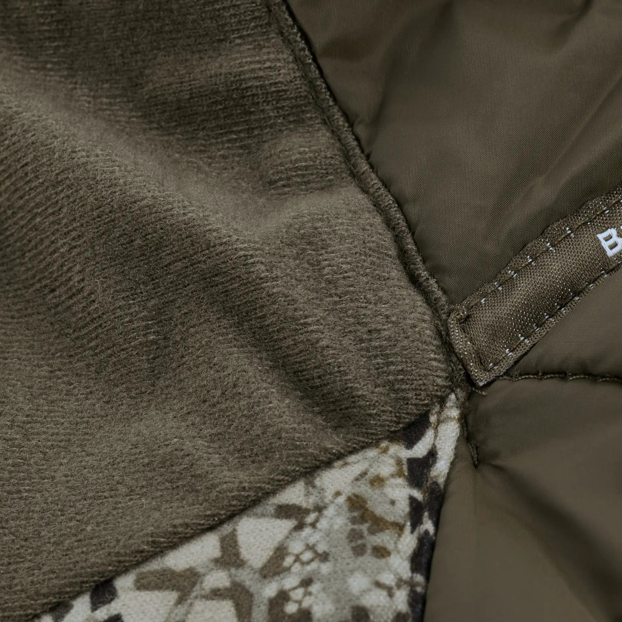 Close-up of Moonrivers hunting jacket fabric showing fleece, camo pattern, and stitched seam with partial Moonrivers logo tag.