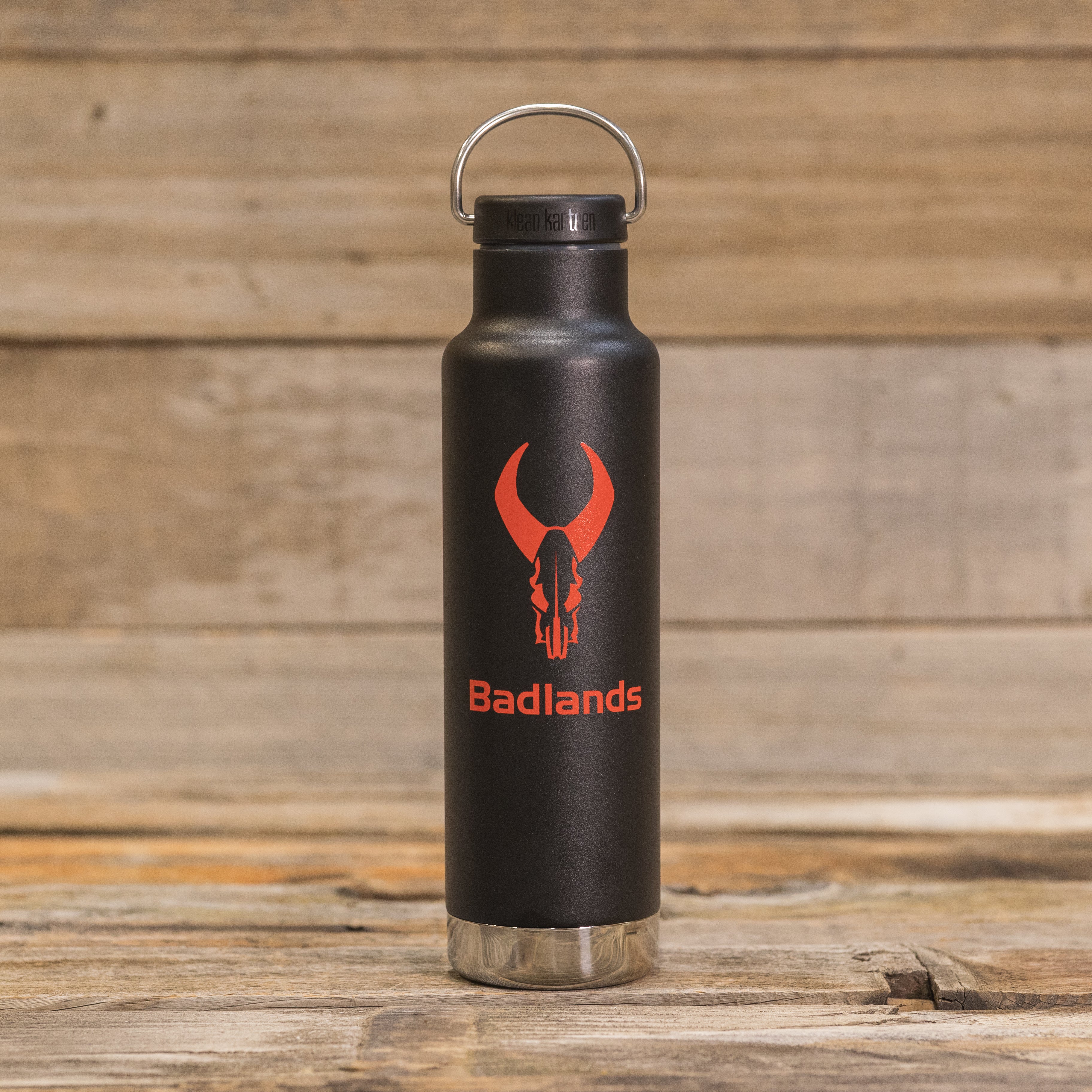 Black water bottle with red Moonrivers skull logo and text, placed on a wooden surface with a metal loop cap.