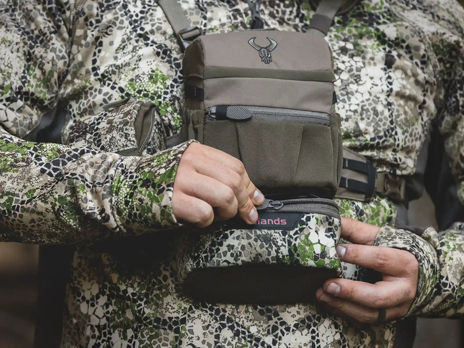 Person in camo gear opens a Moonrivers chest pack with skull logo, designed for outdoor or hunting use.