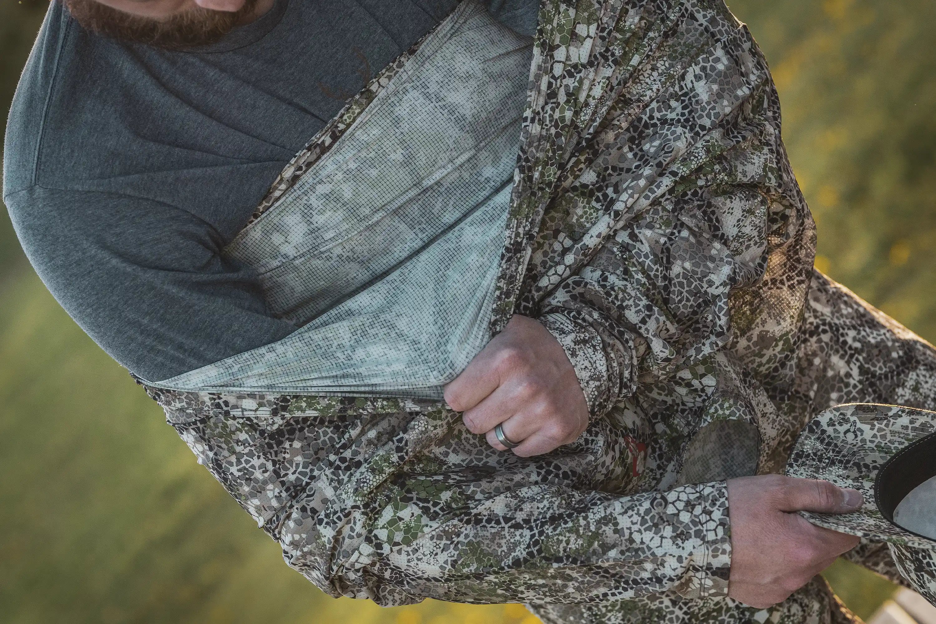 Man wearing Moonrivers camo jacket; visible Moonrivers skull logo on shirt. Outdoor setting, close-up of hands and gear.