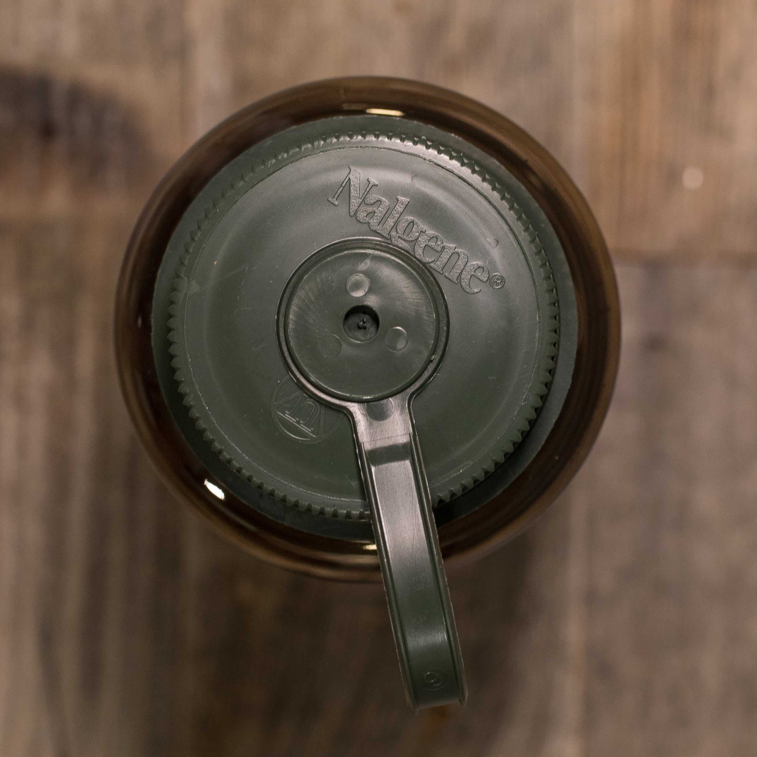 Top view of a green Nalgene bottle lid with textured grip, placed on a wooden surface.