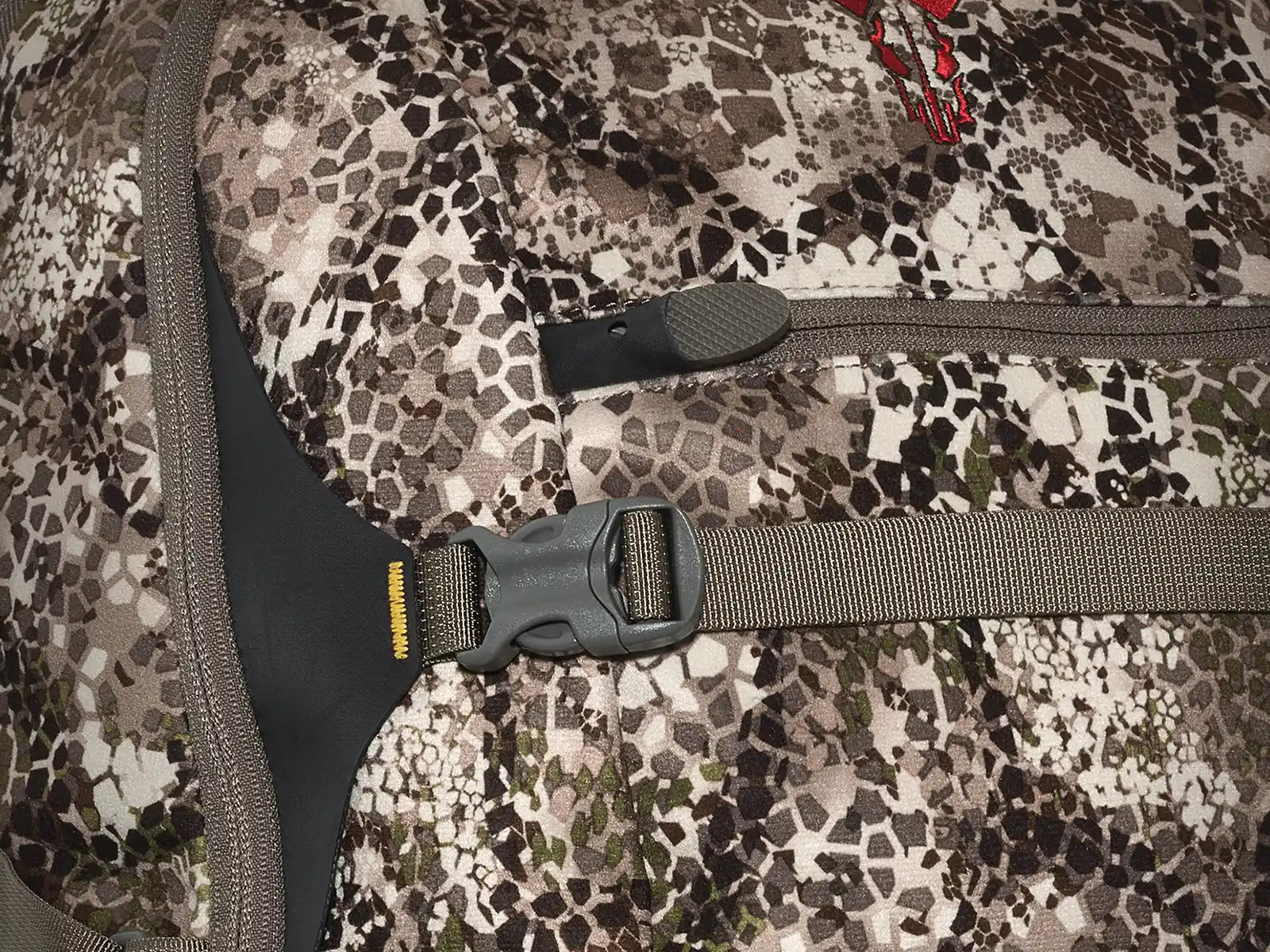 Close-up of a Moonrivers camo backpack with a red skull logo, zipper, and adjustable strap with buckle.