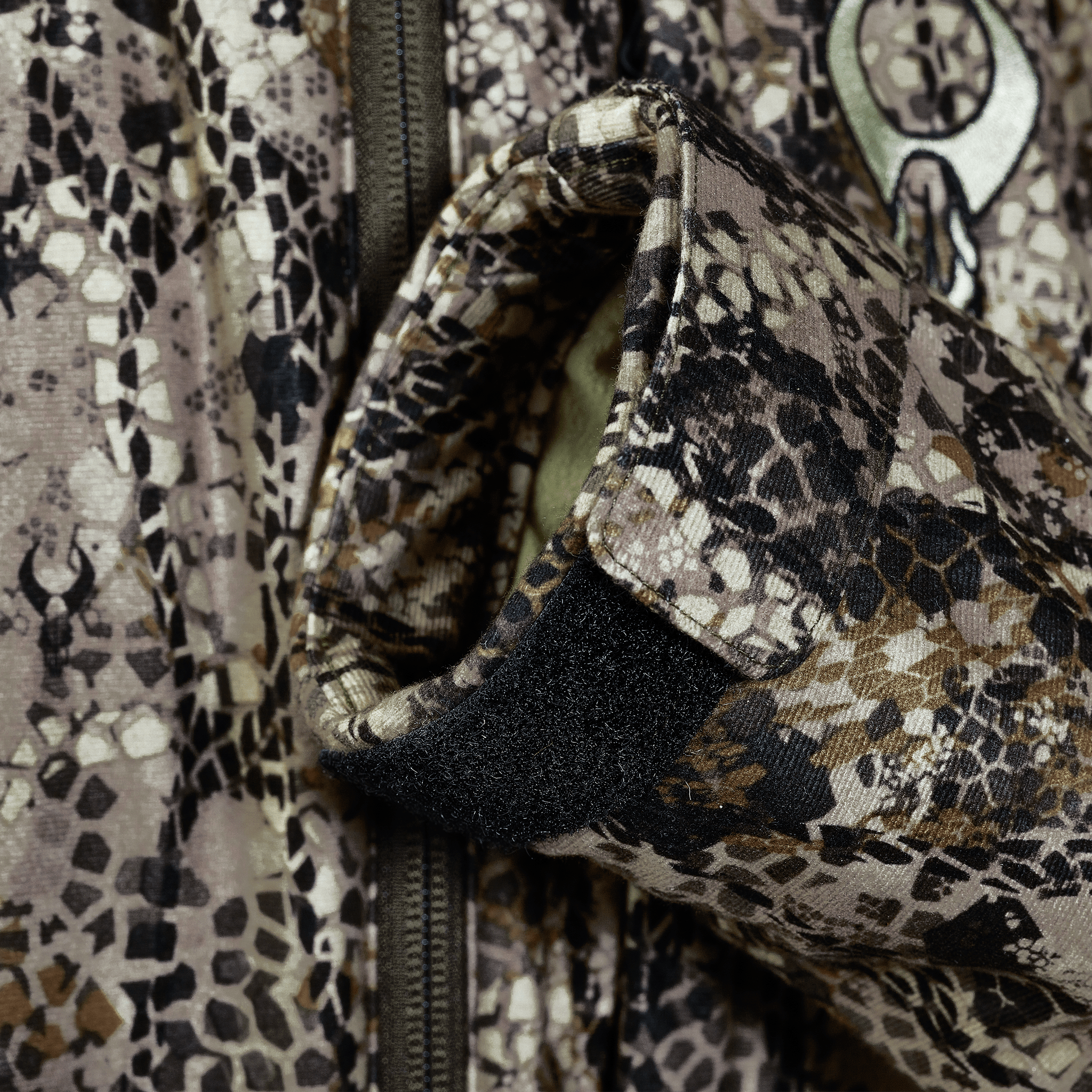 Close-up of a camo jacket sleeve with Velcro cuff and Moonrivers skull logo, showing zipper and textured fabric details.