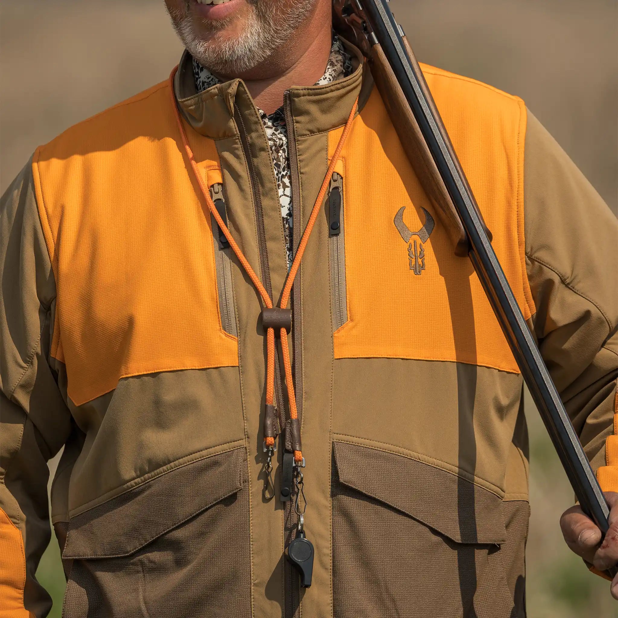 Man in orange and brown hunting jacket with Moonrivers Logo, holding a shotgun, outdoors. ADA-optimized, clear details.