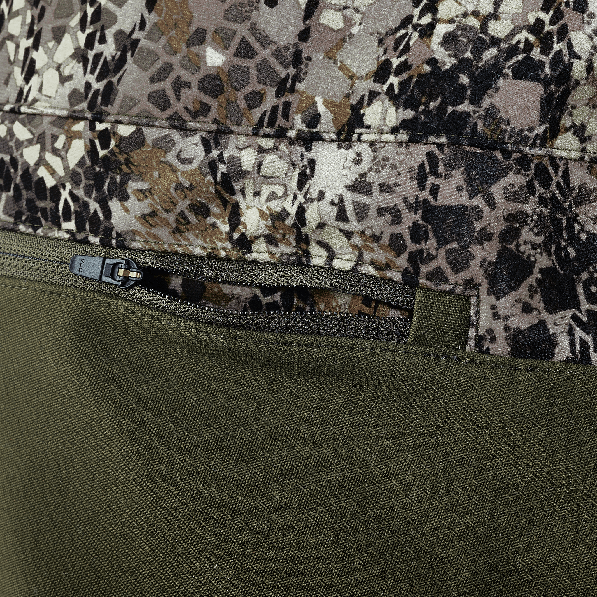 Close-up of a zippered pocket on camouflage fabric with olive green material, showing texture and stitching details.