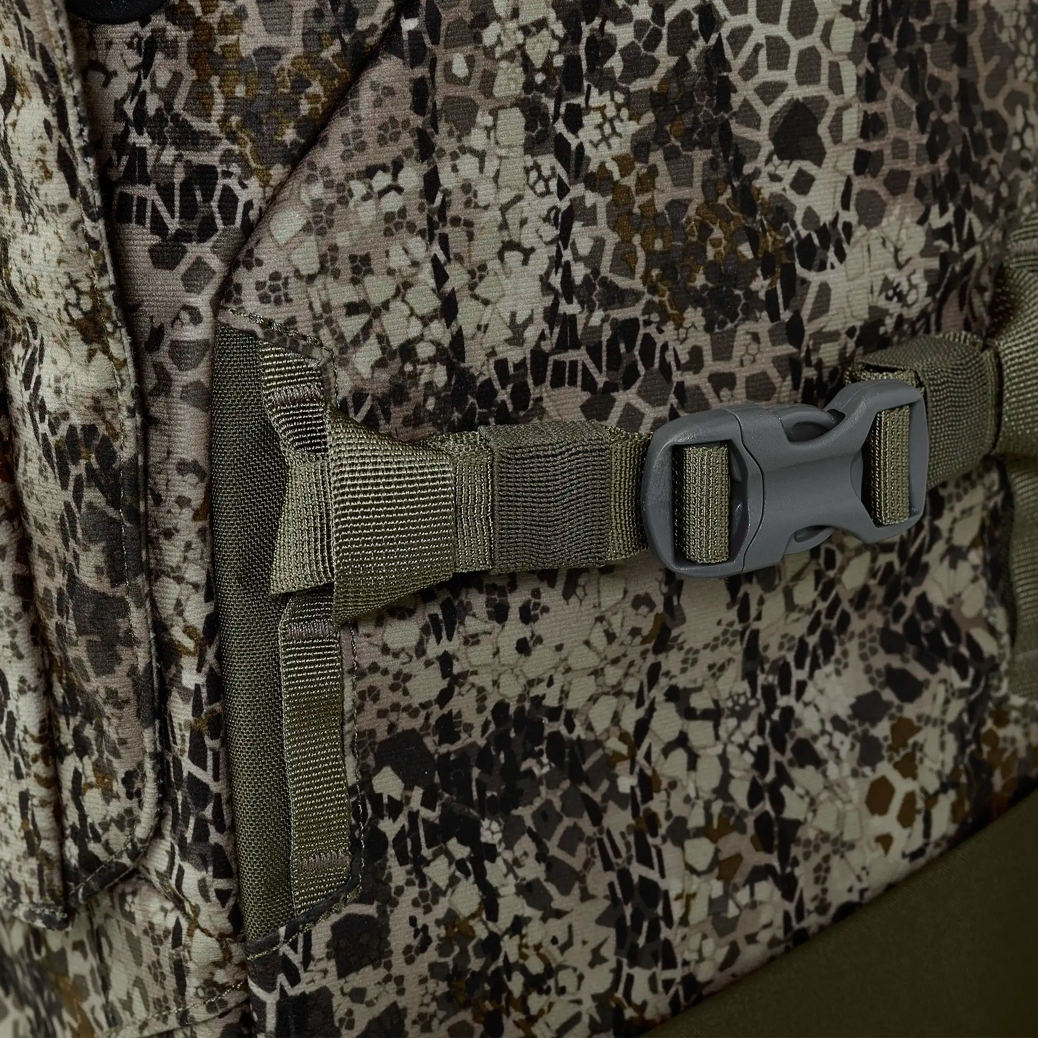 Close-up of a camouflage-patterned backpack with a green strap and plastic buckle, showing detailed stitching and texture.
