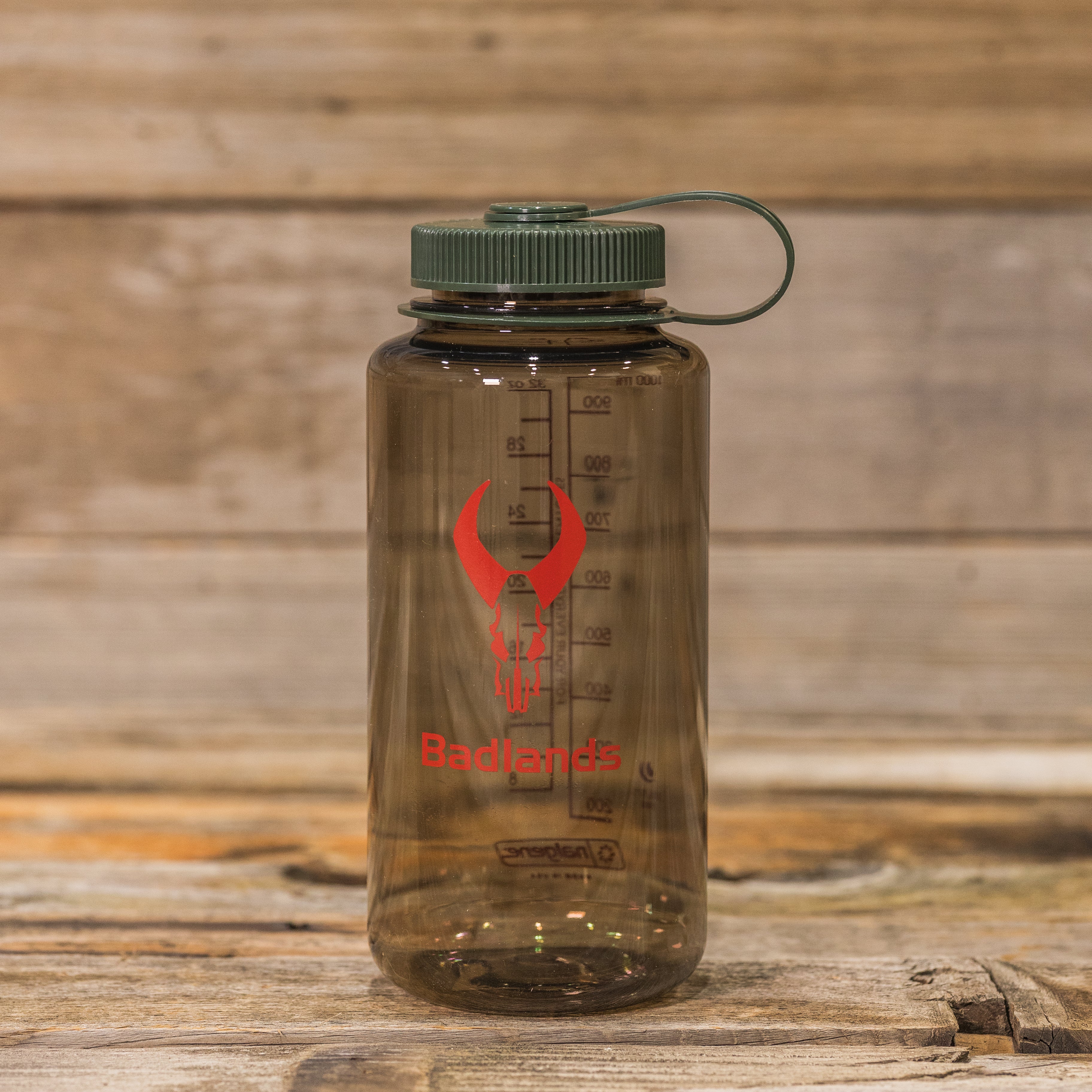 Clear water bottle with green lid, red Moonrivers skull logo, and measurement markings, placed on a wooden surface.
