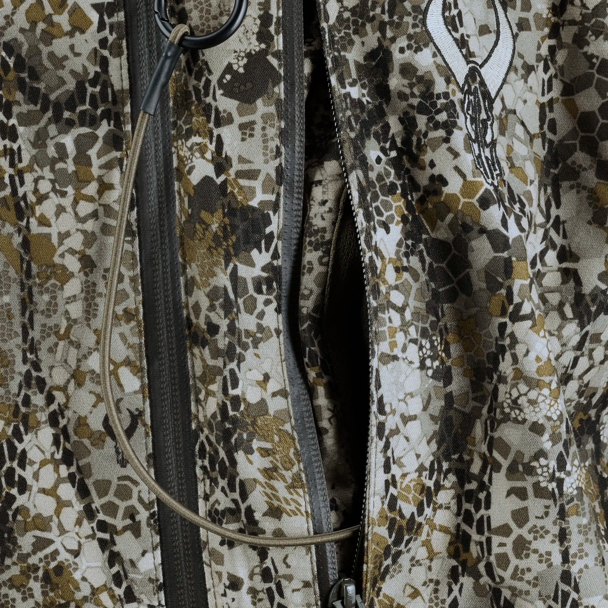 Close-up of Moonrivers camo fabric with zipper, hydration tube, and Moonrivers skull logo in the upper right.
