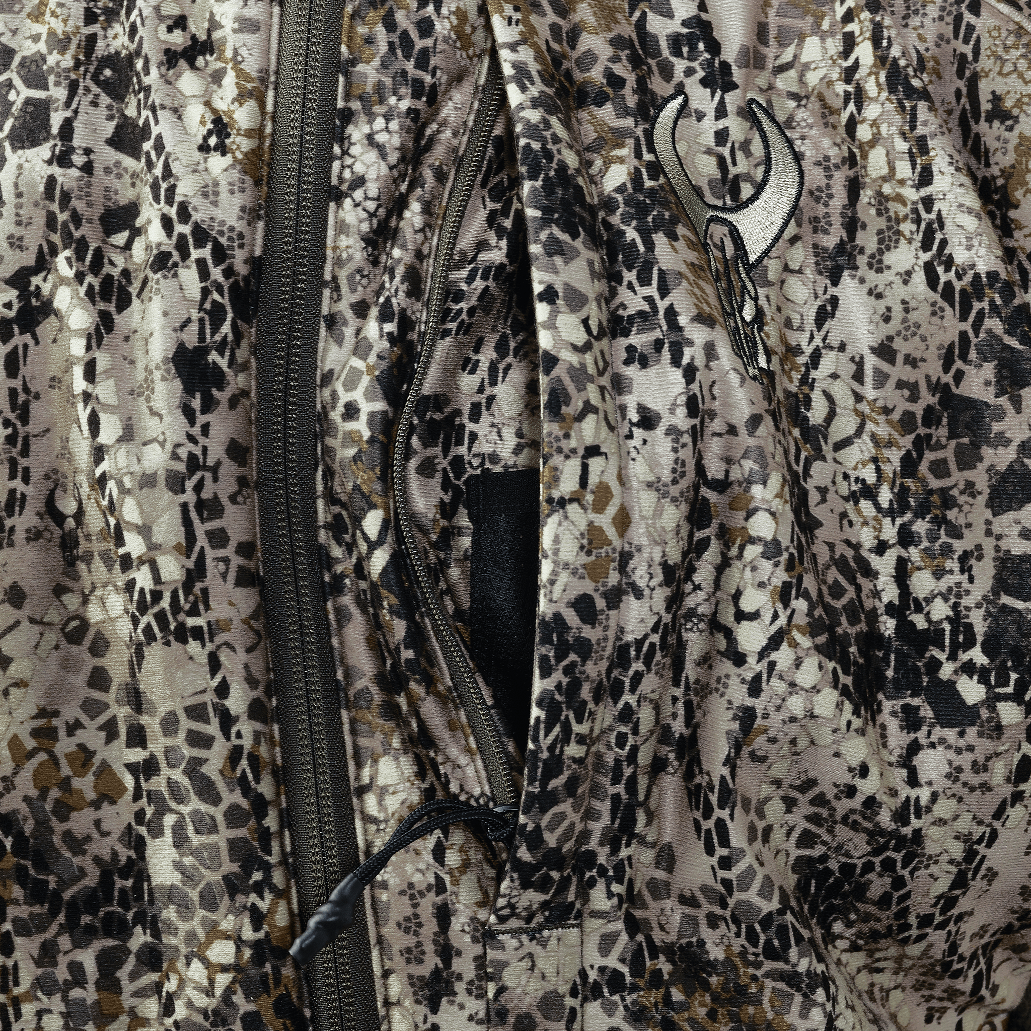 Close-up of camo fabric with a zipper and the Moonrivers skull logo, showing detailed texture and pattern.