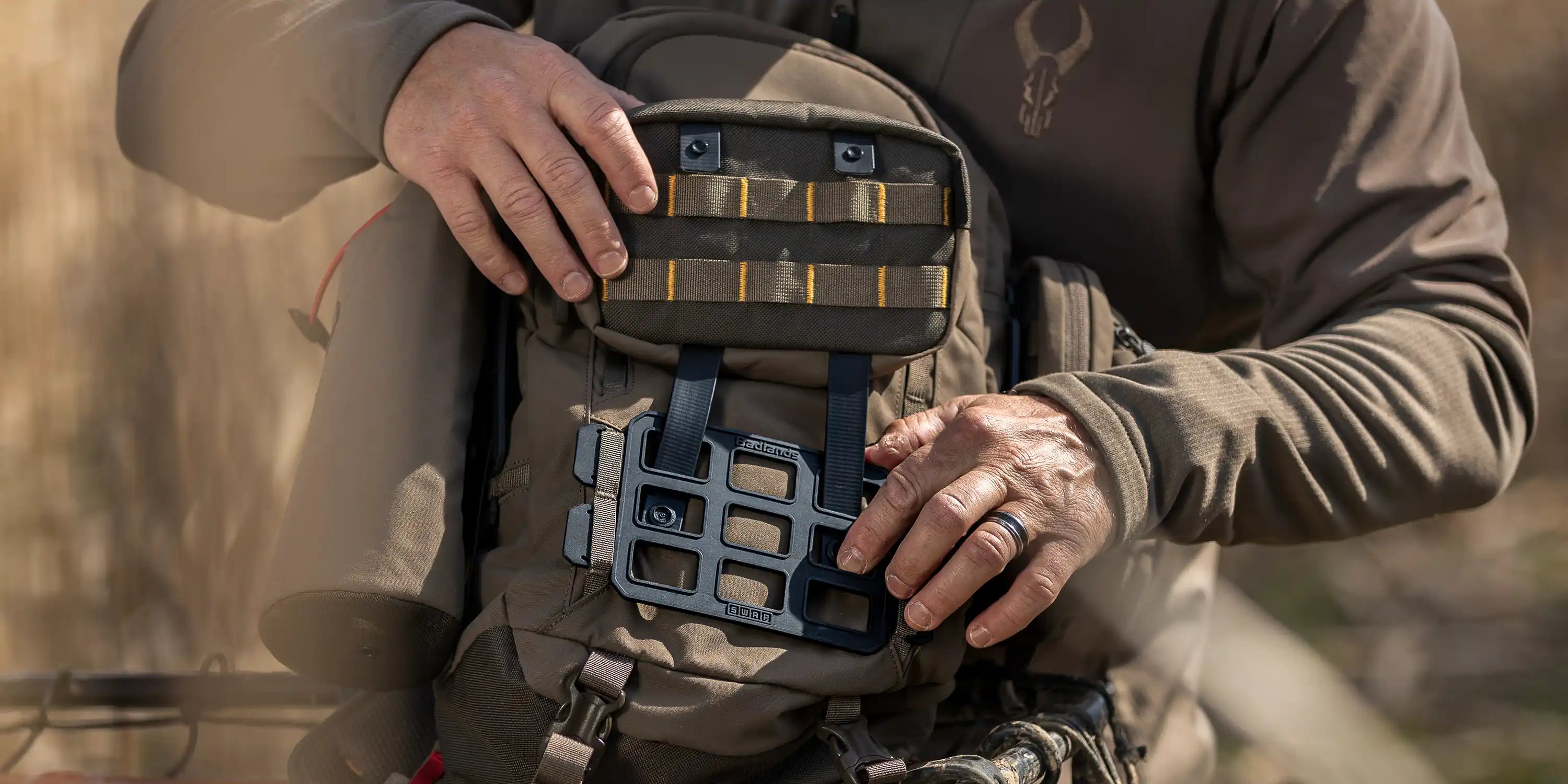 Person attaches gear to a Moonrivers backpack; Moonrivers skull logo visible on jacket. Outdoor setting.