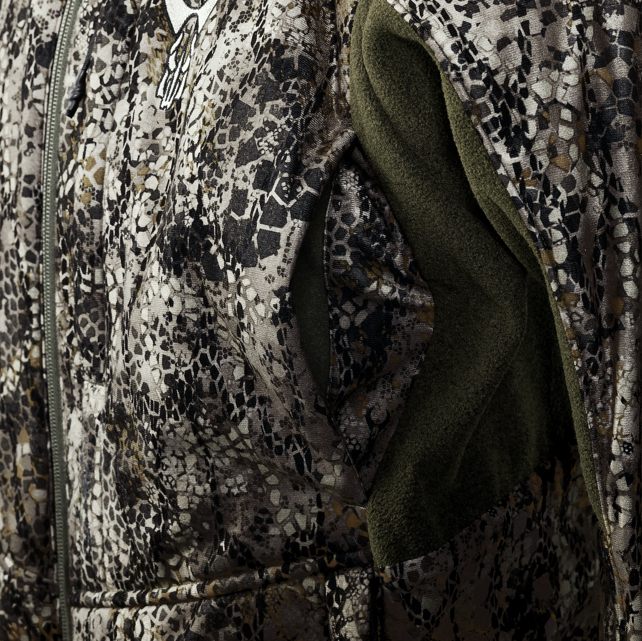 Close-up of a camo jacket with the Moonrivers skull logo and green fleece lining, showing texture and zippered pocket.