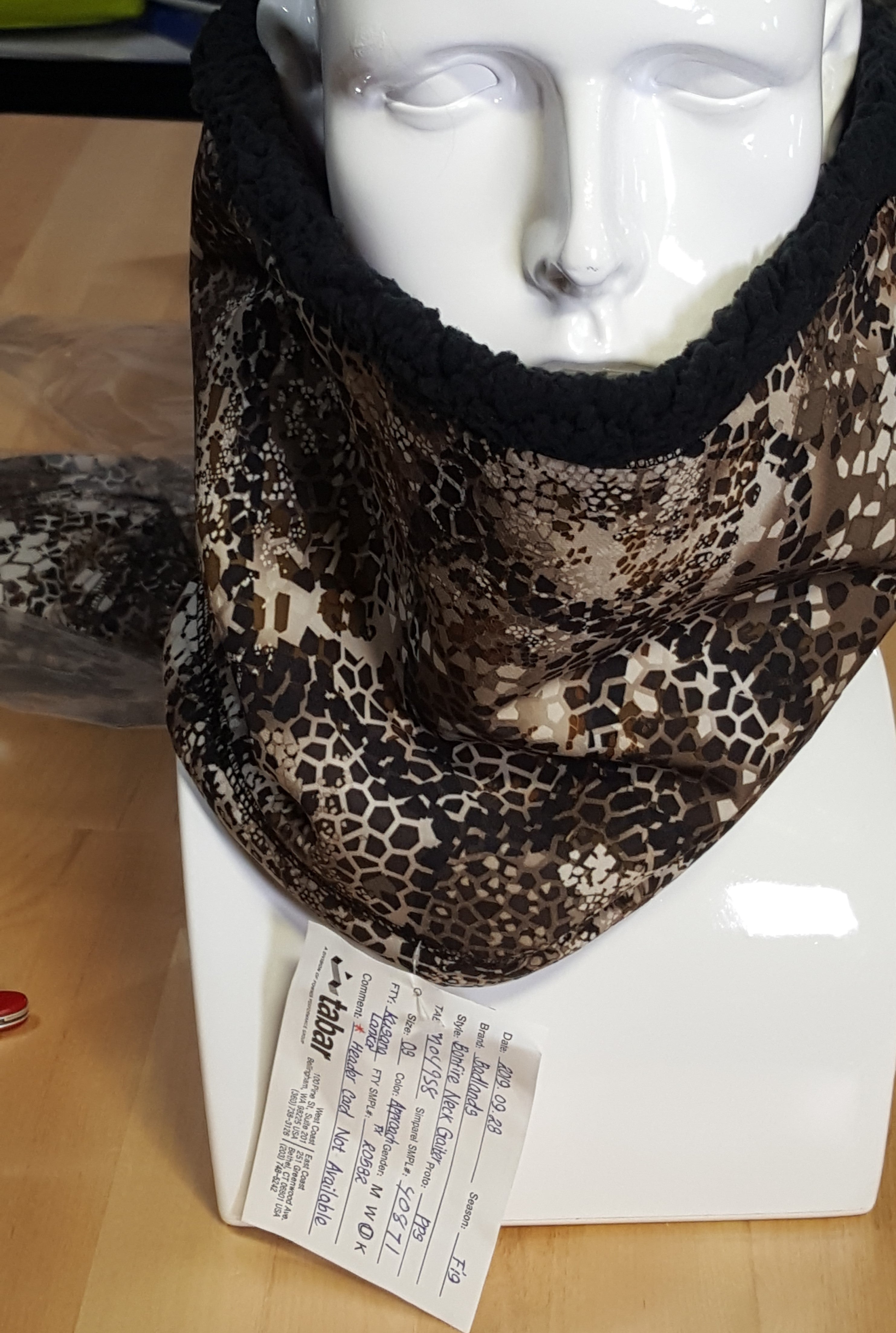 Moonrivers neck gaiter with camo pattern, Moonrivers skull logo tag, displayed on a white mannequin stand.