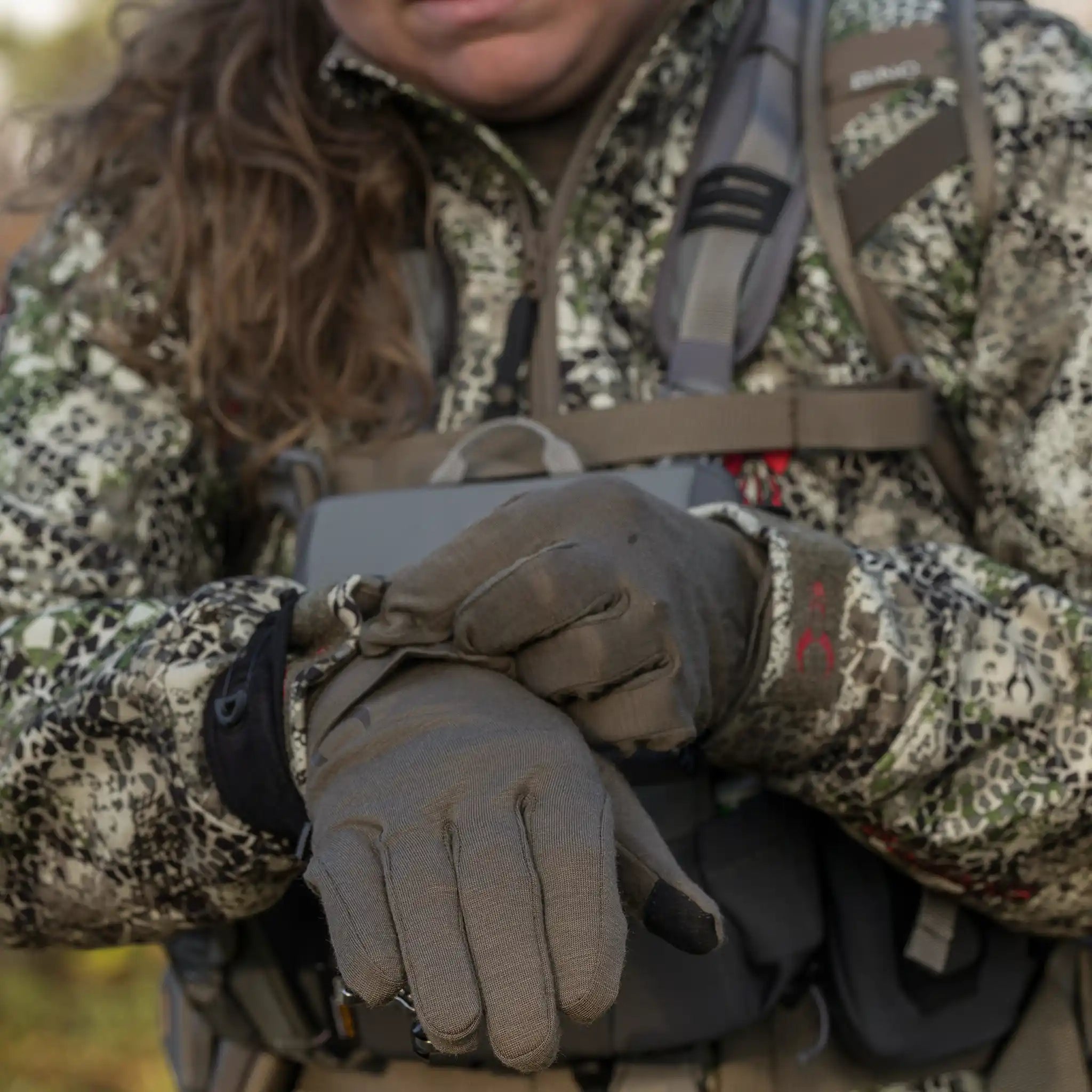 Person in camo jacket and gloves adjusts gear; Moonrivers Logo visible on glove. ADA-optimized, outdoor setting.