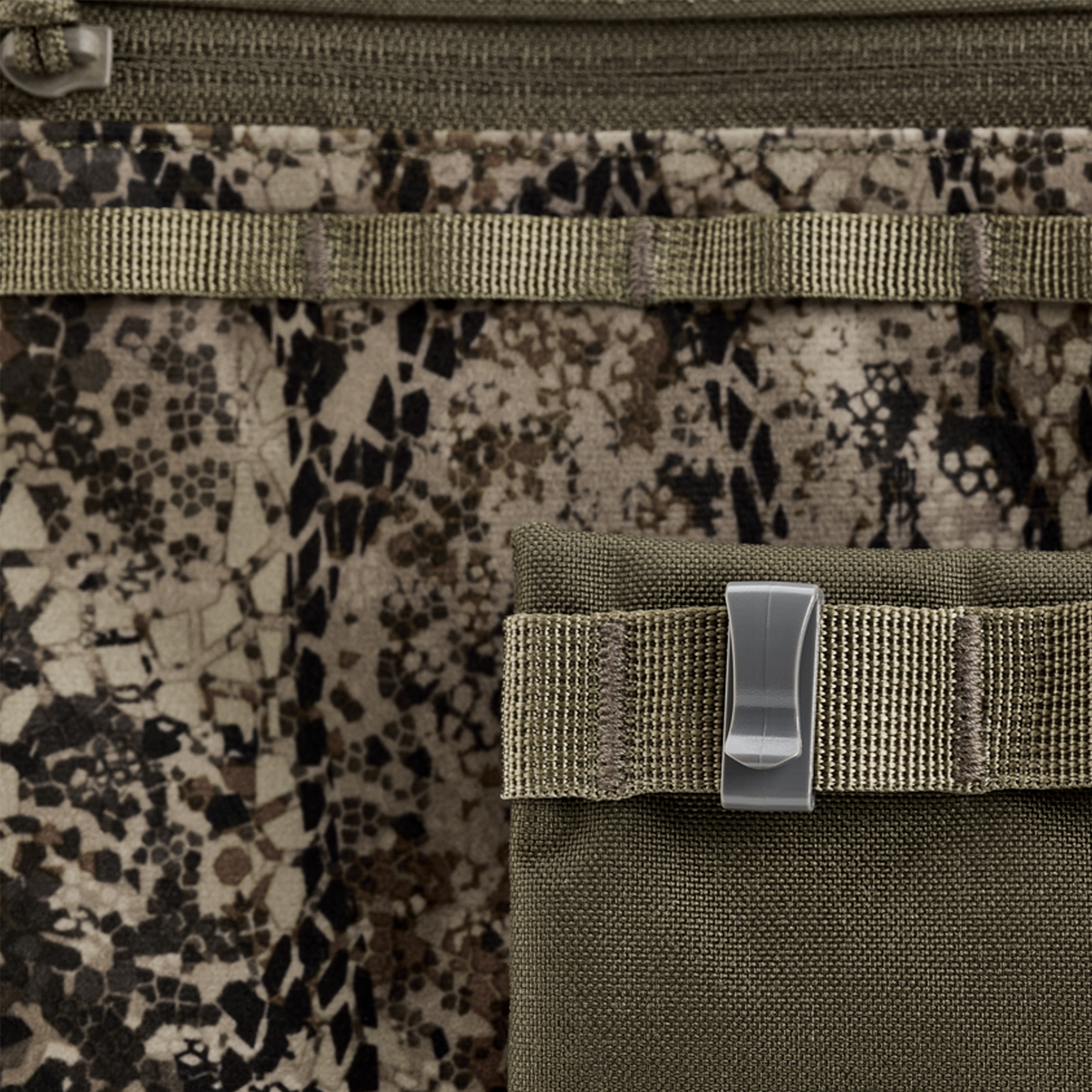 Close-up of camouflage fabric with a green pouch, webbing, and a plastic clip; no visible Moonrivers Logo.