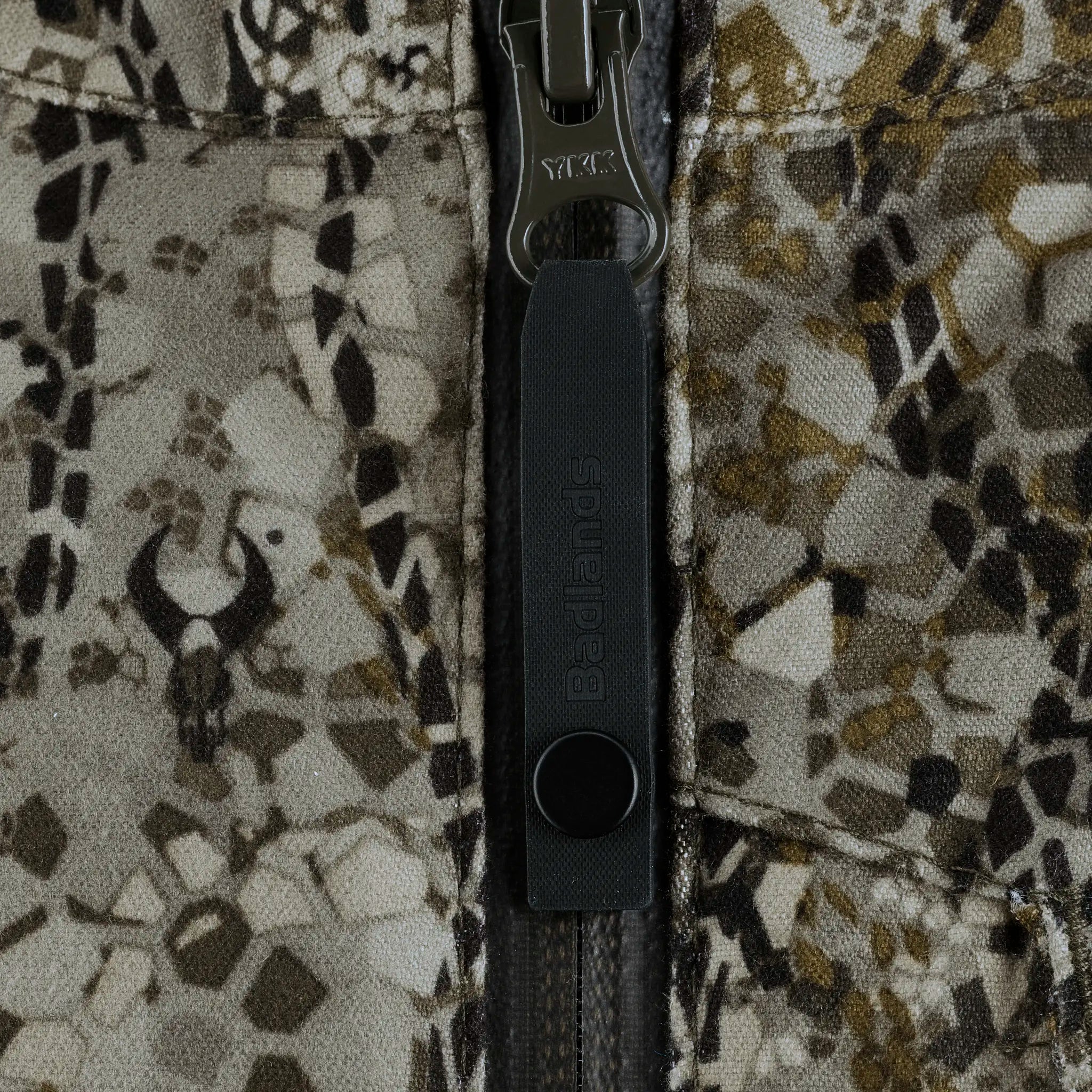 Close-up of Moonrivers camo fabric with zipper and skull logo, showing textured detail and branded pull tab.