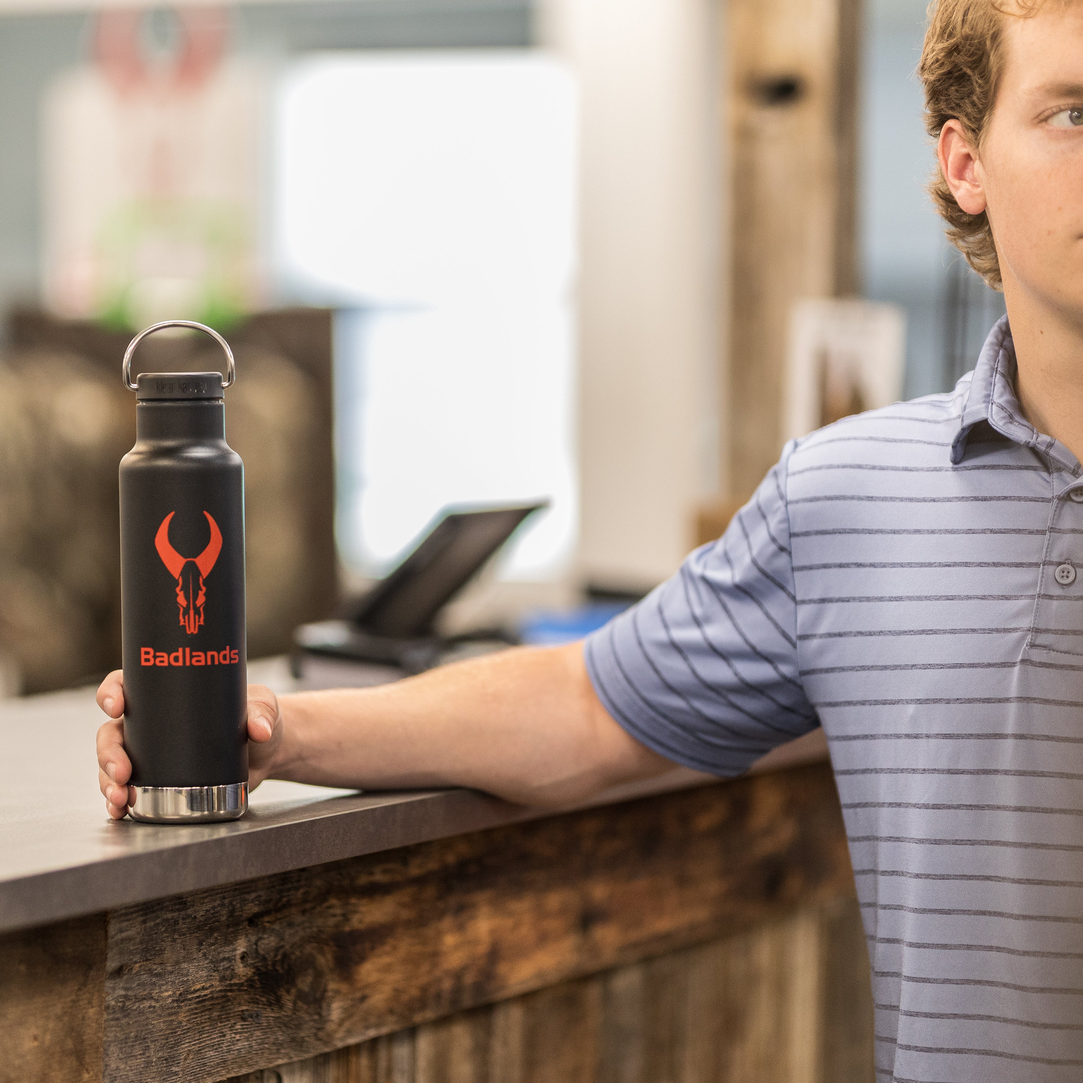 Man in striped shirt holding black water bottle with red Moonrivers skull logo on a wooden counter.