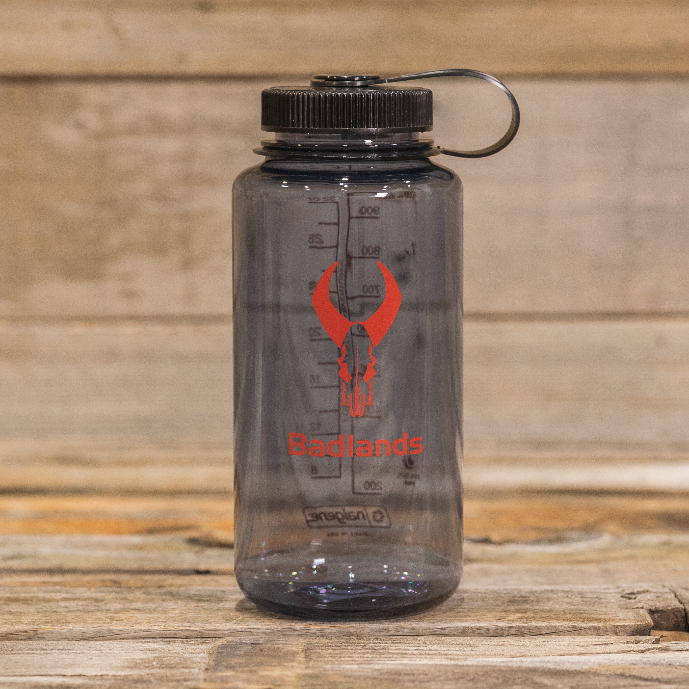 Clear water bottle with black lid, red Moonrivers skull logo, and measurement markings; placed on a wooden surface.