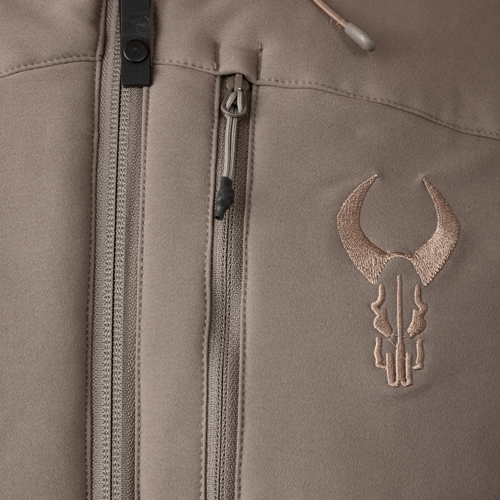 Close-up of a tan jacket with zippers and the embroidered Moonrivers skull logo on the chest.