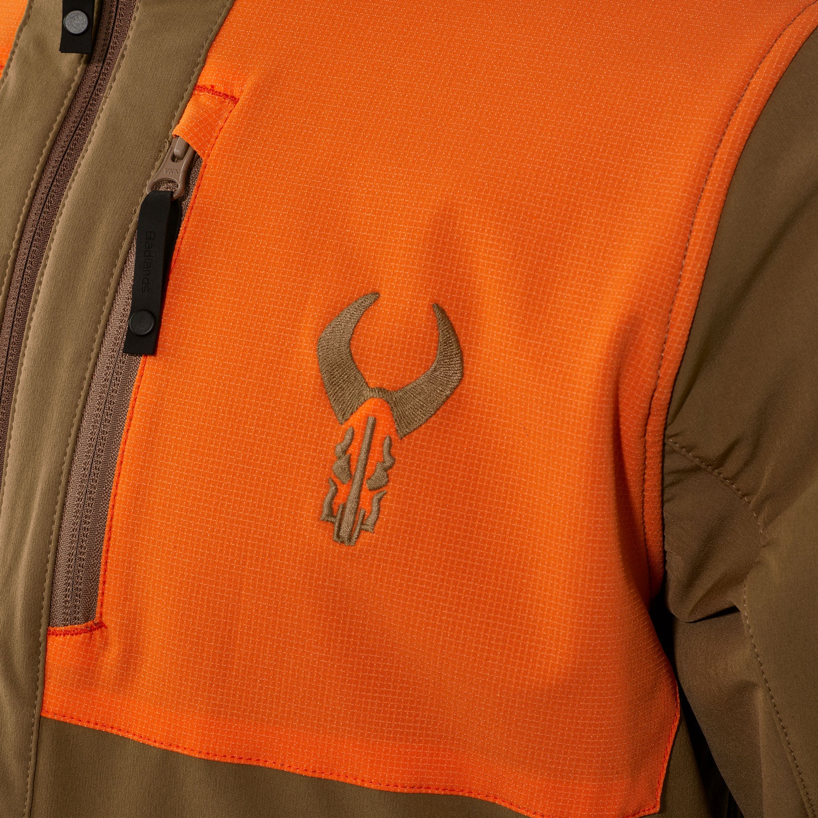 Close-up of orange and brown jacket featuring the Moonrivers skull logo on the chest, with a zippered pocket nearby.